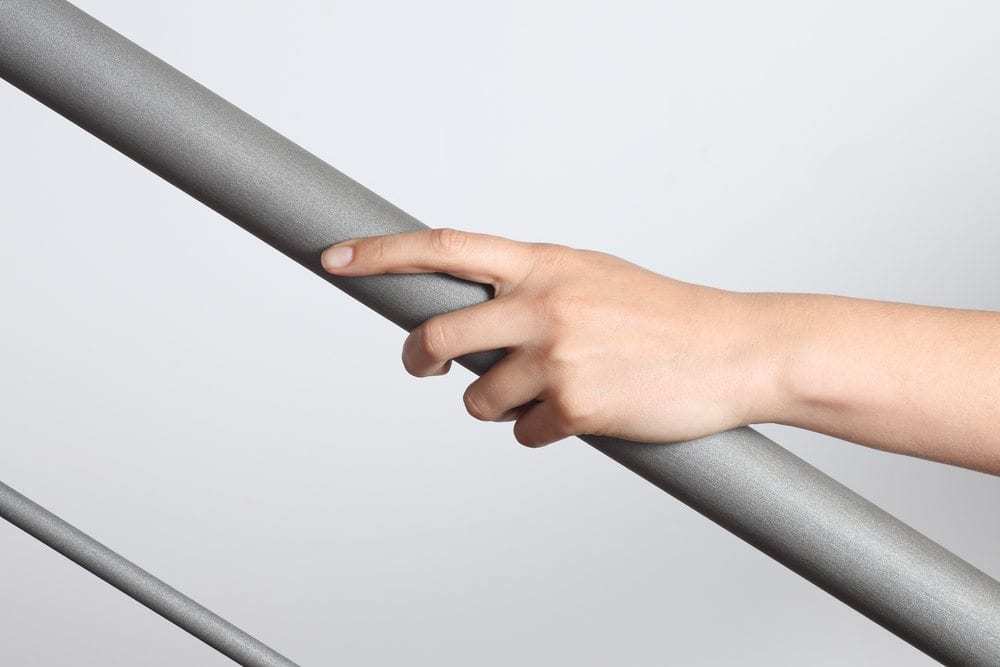 Woman hand using a railing to go upstairs with a light grey background